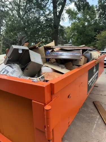 Champs dumpster on a Conway concrete driveway loaded with moving boxes, panel scrap, and an old metal frame under the oaks