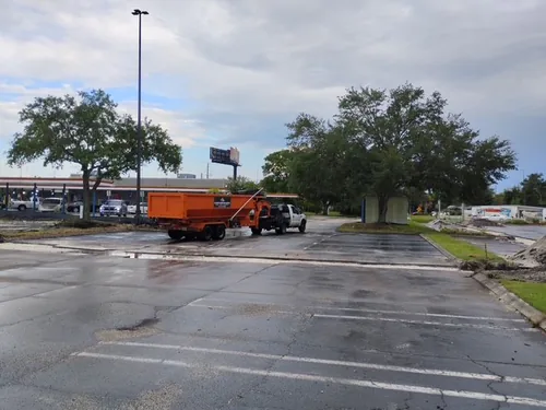 Champs truck towing a dumpster across a wet striped parking lot in Poinciana with a retail plaza and gas station in the background