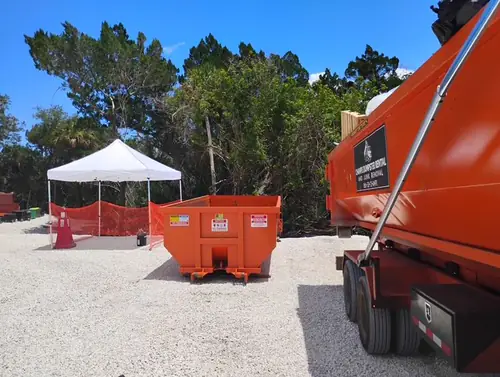 Empty Champs dumpster set on a graded limerock lot in Kissimmee beside a white crew canopy and orange safety fencing