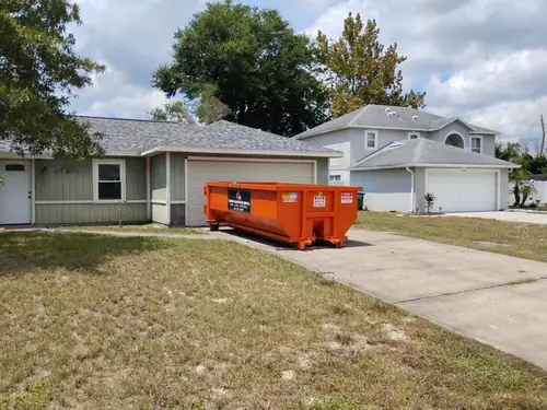 Empty orange Champs dumpster set at the top of an Apopka driveway beside the garage of a sage green board and batten ranch home