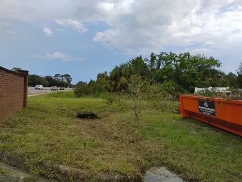 Overgrown Paisley roadside lot before cleanup with the Champs dumpster staged at the far edge
