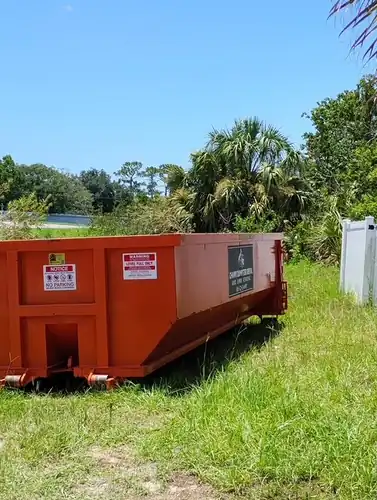 Orange Champs dumpster in the tall grass of a Paisley field with a lake and palms behind