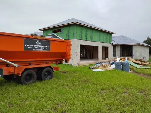 Champs dumpster logo up close with the Groveland build and a debris pile behind it