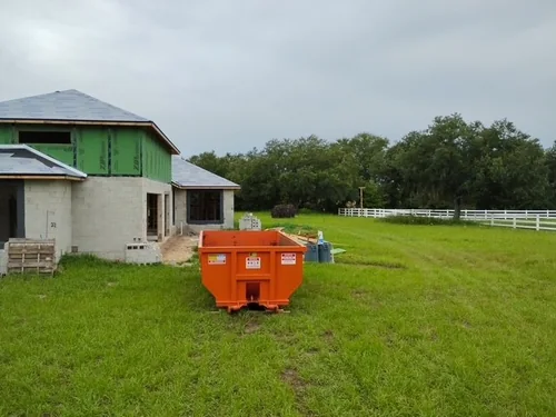 Orange Champs dumpster on the grass in front of the framed Groveland new construction home