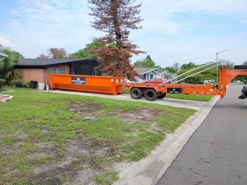 Orange Champs dumpster and trailer on the driveway beside a brick ranch home in Mims