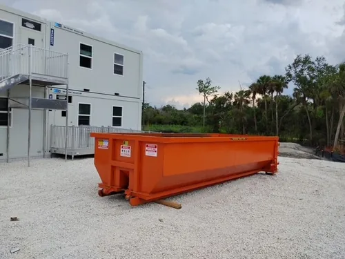 Orange Champs dumpster set on the gravel commercial lot with the office trailers alongside