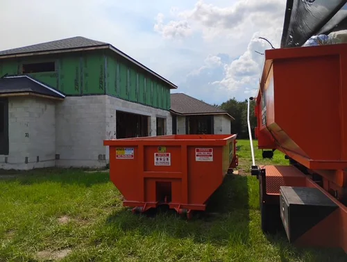 Champs dumpster set on grass beside a two story Kissimmee home under construction with block walls and green sheathing