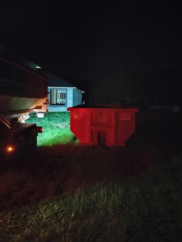 Champs dumpster resting on grass at a Kissimmee construction site with the block shell behind it in the dark