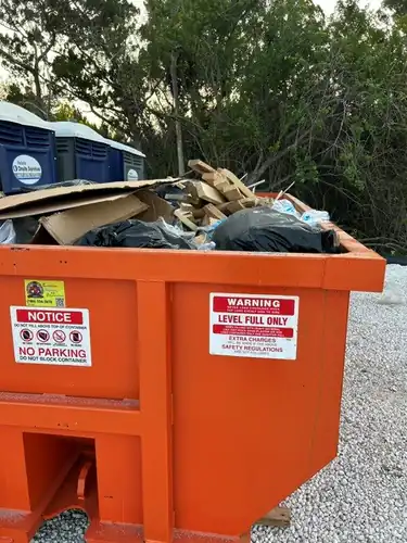 Close view of the LEVEL FULL ONLY warning decal on a Champs dumpster loaded to the rim with lumber and contractor bags