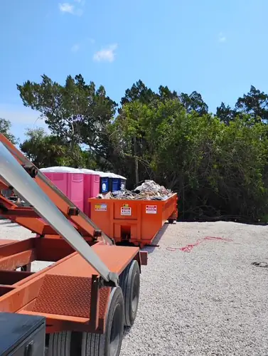 Champs dumpster loaded level with lumber offcuts and bagged debris beside the portable toilets on the Eustis job site