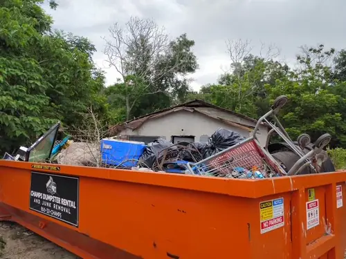 Loaded Champs dumpster on a Deltona lot with a derelict block house and collapsed roof behind it during a property cleanout