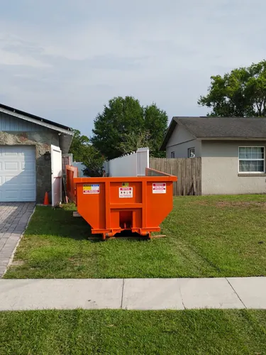 Champs dumpster set on the side lawn beside a paver driveway and wood privacy fence gate at a Lake Mary home