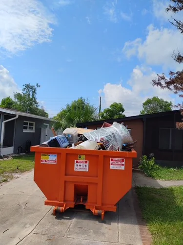 Loaded Champs dumpster on a Longwood driveway holding a wrapped mattress, patio chairs, and lumber from a garage cleanout