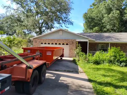 Champs dumpster set outside the arched garage doors of a brick ranch home at the end of a long Ocoee driveway