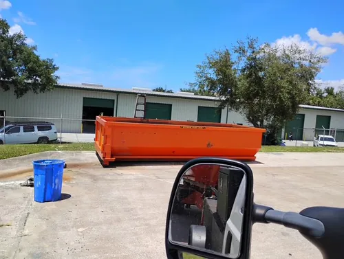 Champs dumpster set on the concrete apron in front of the green warehouse bays at a Winter Springs commercial yard