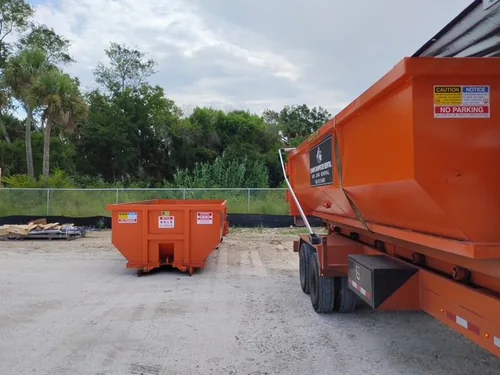 Empty Champs dumpster set on packed sand near the chain link fence with a second bin still on the trailer
