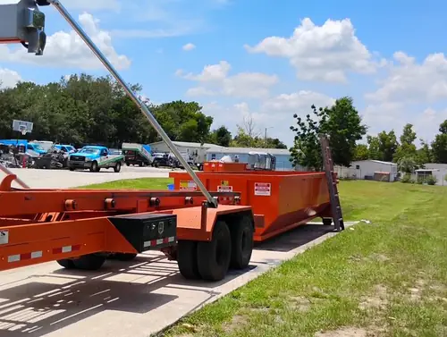 Champs roll off trailer with the hoist arm raised as a dumpster is lowered at the edge of the Winter Springs equipment yard